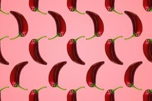 Pattern of red peppers isolated on pink background. Creative photo of peppers aligned with copy space.