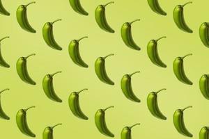 Pattern of green peppers isolated on light green background. Creative photo of peppers aligned with copy space.