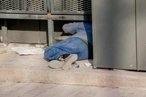 A homeless man sleeps outside in the shade of a building photo