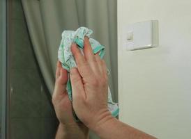 una mujer limpia un espejo con una servilleta de suciedad y placa del agua en casa foto