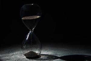 reloj de arena sobre fondo oscuro, primer plano. concepto de urgencia y agotamiento del tiempo foto