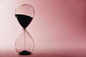 Hourglass on pink background, closeup. Urgency and running out of time concept photo