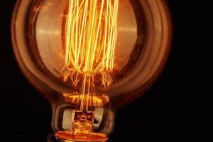 Vintage light bulb on black background, closeup. Glowing edison bulb photo