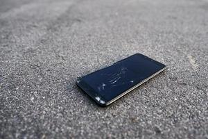Damaged smartphone with broken touch screen on asphalt photo