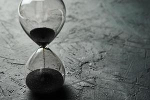 Hourglass on dark background, closeup. Urgency and running out of time concept photo