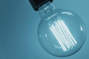 Vintage light bulb on blue background, closeup. Glowing edison bulb photo