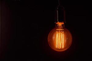 Vintage light bulb on black background, copy space. Glowing edison bulb photo