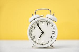Time concept. White retro alarm clock on yellow background with copy space photo