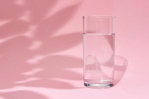 Glass of water and leaf shadow on a pink background photo