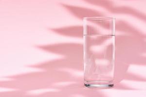 vaso de agua y sombra de hojas sobre un fondo rosa foto