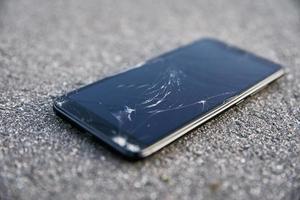 Damaged smartphone with broken touch screen on asphalt photo