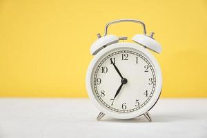 Time concept. White retro alarm clock on yellow background with copy space photo