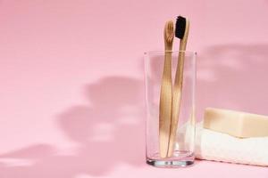 Bamboo toothbrushes in the glass and leaf shadows on pink background photo