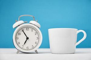 White retro alarm clock and cup on blue background. Morning time concept photo