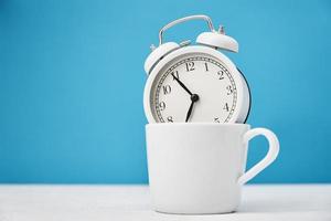 White retro alarm clock in cup on blue background. Morning time concept photo