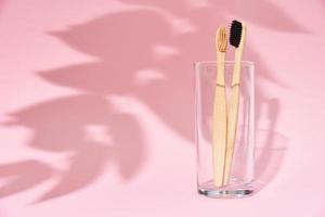 Bamboo toothbrushes in the glass and leaf shadows on pink background photo