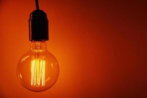 Vintage light bulb on orange background, copy space. Glowing edison bulb photo