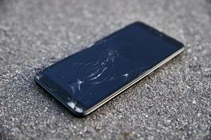 Damaged smartphone with broken touch screen on asphalt photo