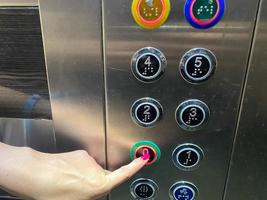 el dedo cuidado de una mujer en su mano presiona un botón en un moderno y hermoso ascensor en un edificio de gran altura foto