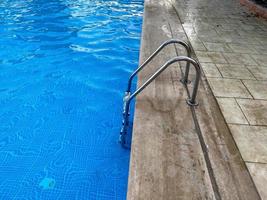 escalera de metal cromado con barandilla para descender a la piscina para nadar y bañarse con agua tibia azul clara y limpia en un hotel en un paraíso tropical foto