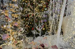 shop window decoration, shopping center decor. artificial white spruce with garlands. next to trees with long light garlands. light illumination, bright balls photo