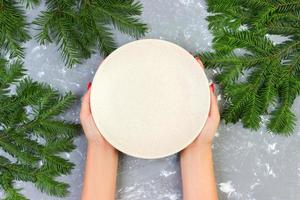 female hands holding an empty white plate on a gray background with Christmas branches. view from above for your design photo