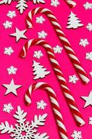 Christmas candy cane lied evenly in row on pink background with decorative snowflake and star. Flat lay and top view photo