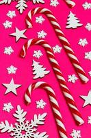 Christmas candy cane lied evenly in row on pink background with decorative snowflake and star. Flat lay and top view photo