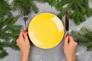 Hungry woman waiting for meal. empty yellow plate on a gray background with Christmas branches. view from above for your design photo