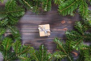 Frame of pine branches. Gift wrapped in kraft paper, decorated with ribbon and bow in silver color. Christmas New Year decorations Black background, top view, flat lay, copy space photo