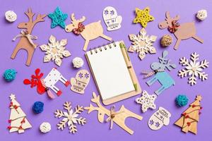 Festive decorations and toys on purple background. Top view of notebook. Merry Christmas concept photo