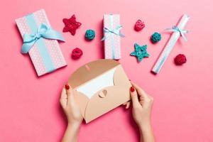 Top view of woman holding an envelope on pink background made of holiday decorations. Christmas time concept photo