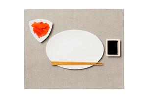 Empty oval white plate with chopsticks for sushi, ginger and soy sauce on grey napkin background. Top view with copy space for you design photo