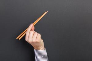 Cropped image of male hand holding chopsticks on black background. Asian food concept with copy space photo