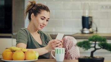 kvinna använder sig av smartphone och dricka kaffe i de morgon- på Hem video