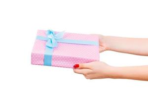 Woman hands give wrapped Christmas or other holiday handmade present in pink paper with blue ribbon. Isolated on white background, top view. thanksgiving Gift box concept photo