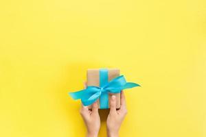 Woman arms holding gift box with blue ribbon on color background, top view photo