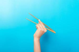 Female hand with chopsticks on blue background. Traditional asian food with emty space for your design photo