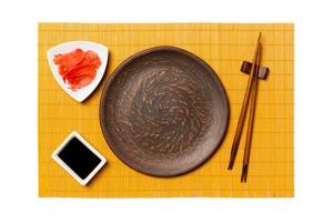 Empty round brown plate with chopsticks for sushi, ginger and soy sauce on yellow bamboo mat background. Top view with copy space for you design photo