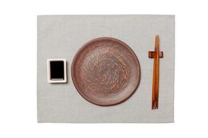 Empty round brown plate with chopsticks for sushi and soy sauce on grey napkin background. Top view with copy space for you design photo