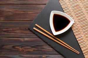 Chopsticks and soy sauce on black stone plate, wooden background with copy space photo