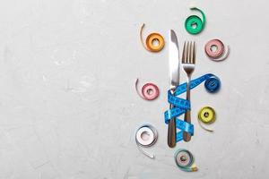 composición de cintas métricas de colores, tenedor y cuchillo sobre fondo de cemento con espacio vacío para su diseño. concepto de sobrepeso foto