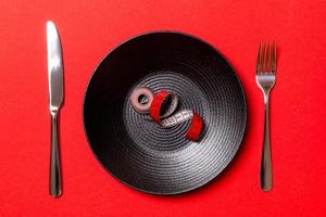 Healthy diet concept of plate with measuring tape, fork and knife on red background. Top view photo