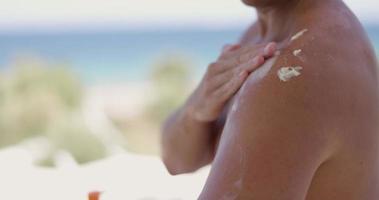 dichtbij omhoog van een Mens toepassen zonnebrand lotion naar zijn schouder. video
