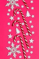 Christmas candy cane lied evenly in row on pink background with decorative snowflake and star. Flat lay and top view photo