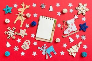 Top view of notebook, holiday toys and decorations on red Christmas background. New Year time concept photo