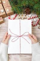 Top view of christmas letter in hand. Close up of hands holding empty wishlist on wooden table with xmas decoration photo