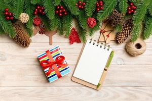 Top view of gift, notebook, Christmas toys, decorations and fir tree branches on wooden background. New Year holiday concept photo