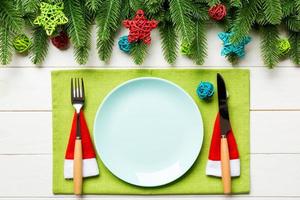 Top view of fork, knife and plate surrounded with fir tree and Christmas decoratoins on wooden background. New Year Eve and holiday dinner concept photo