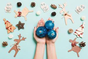 vista superior de un montón de bolas de año nuevo en manos femeninas sobre un fondo azul hecho de decoraciones festivas. concepto de tiempo de navidad foto